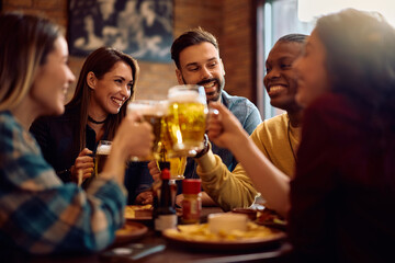 Group of happy friends drinking beer and toasting while gathering in pub.