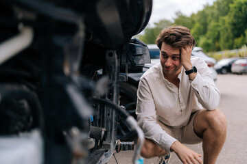 Unhappy young driver man assesses damage to car following accident on street, concerned about...