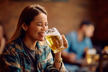 Cheerful woman having a beer while sitting in pub.