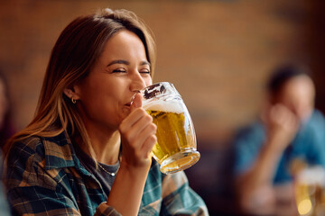 Happy woman drinking beer in bar.