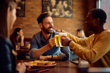 Happy male friends toasting while drinking beer in pub.
