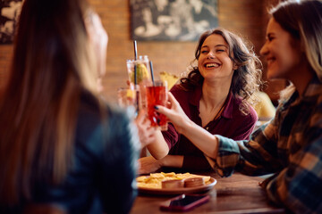 Young happy women toasting while gathering in pub.