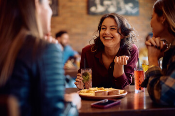 Cheerful woman talking to her female friends while gathering for drink in bar.