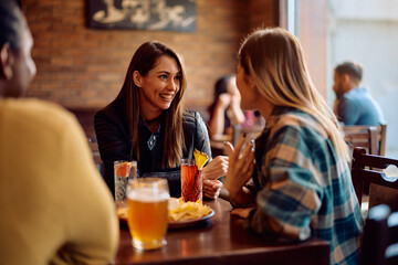 Happy female friends talking while gathering in pub.
