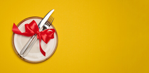 Round white plate and tied with red bow view with knife on yellow background, festive table setting