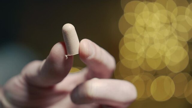 Person holding ear plug against Christmas lights bokeh background, holiday noise protection macro, peaceful celebration concept