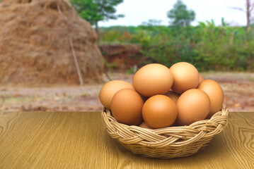 Chicken eggs are in a basket and placed on the table. The background is a farm.