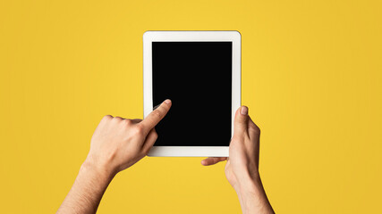 Young man touching blank screen of tablet computer on light background, closeup. Mockup for design. Panorama