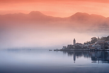 Scenic view of a coastal town at sunrise with fog rolling in and mountains in the background