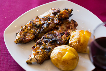 Appetizing grilled pettitoes served on white plate with baked whole potatoes..