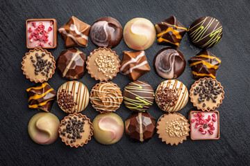 Mix of chocolate pralines on black table. Top view.