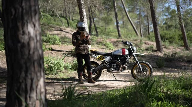 Hombre aventurero en moto de campo por el bosque de dia tomando fotos y videos