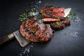 Barbecue dry aged raw beef steaks - entrecote cut medium roasted served as close-up with herbs and...
