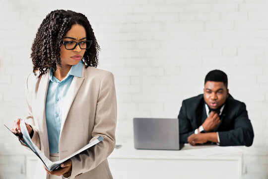 Sexual intimidation concept. Perverted black businessman looking at his female colleague from behind at office, free space. Young lady feeling stressed from her male coworker's ogling