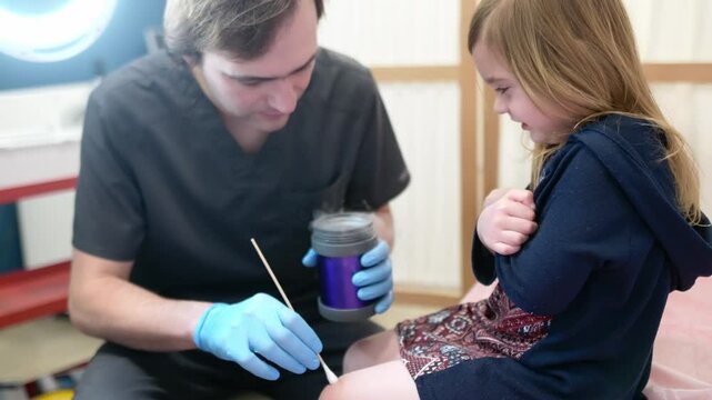 A caring doctor checks moles and warts on the skin of a small child. Dermatologist remove of benign tumors with liquid nitrogen for cute preschooler girl. Baby fears of treatment.