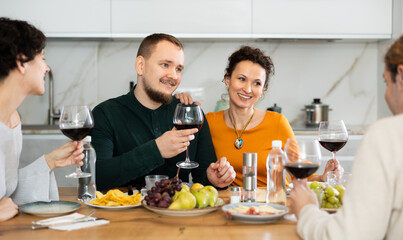 Two married couples are sitting at table, enjoying food and wine, chatting, talking, laughing. In homely atmosphere, friends celebrate anniversary