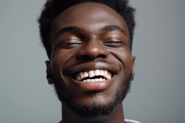 Obraz premium Close up portrait of a happy young african american man laughing against gray background