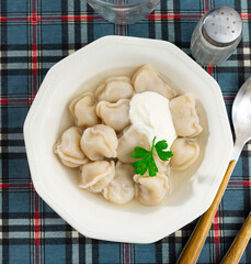 Delicious Russian pelmeni traditionally served on plate in broth with sour cream garnished with greens