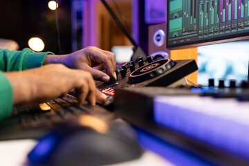 Skilled artist audio engineer mixing and mastering tracks on stereo console, operating with...