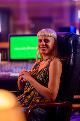 Portrait of female music producer sitting at neon lit music studio.