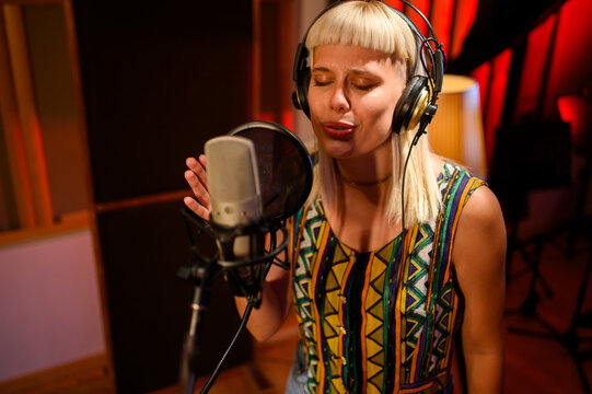 Professional blond vocalist with headphones singing into mic at studio - Powered by Adobe