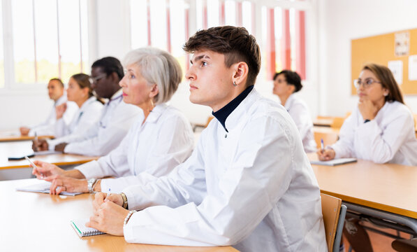 Portrait of focused young medical intern listening to lecture at university for professional development with mixed age group of colleagues of different nationalities..