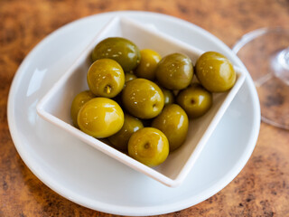 In small bowl there are pickled green olives. Traditional vegetable addition to main dishes, snacks and alcoholic beverages