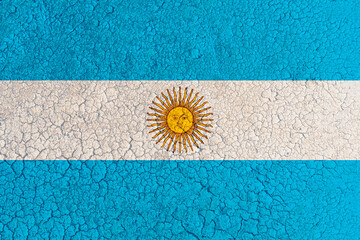 Cracked clay lake bed with Argentina flag painted on it (close-up). Concept of climate change, drought and water drying up in Argentina