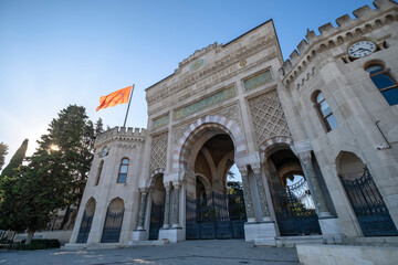 main entrance of the university of istanbul with the waving flag of turkey backlit against a blue sky, sunbeams filtering through the trees