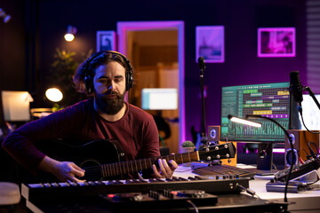 Music engineer recording songs and playing acoustic guitar, working in his personal home studio to...