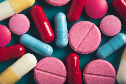Assorted colorful pills and capsules on a teal background - Powered by Adobe