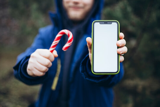 Man holding candy cane and smartphone with blank screen