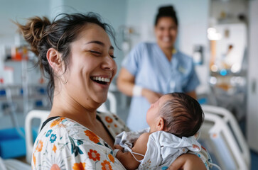 Smiling mother holding her newborn baby in a hospital room, with a nurse in the background