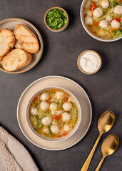Food photography of soup with chicken meatballs and  vegetables, carrots, cabbage, broccoli, potatoes, bell pepper, broth, toasted bread, spring onion, sour cream