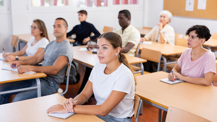 Fototapeta premium Young caucasian woman sitting at table in classroom during lesson with group of students.