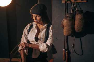 Caucasian woman in a Peaky Blinders style men's suit posing in a retro gym.