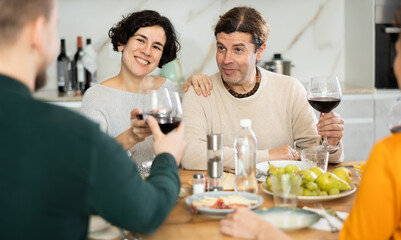 Group of joyful individuals are celebrating a holiday, enjoying drinks and conversation around a table in their home