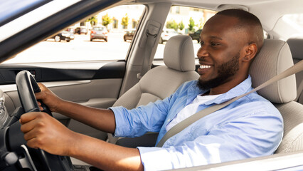 Happy African American young man driving new auto, going to office or on vacation, shot from...