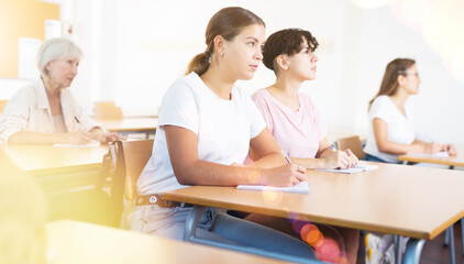 Portrait of focused young attractive girl attending lecture as part of graduate education with mixed age group