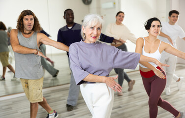 Cheerful old lady learning new modern dance in group dance lesson
