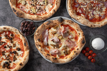 top view group of various pizzas, with ingredients, mozzarella, olives and cherry tomatoes. On dark background