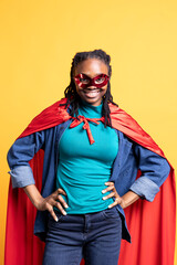 African american girl wearing superhero costume and mask for Halloween, placing hands on hips, studio background. Portrait of woman dressed as comic book hero hiding identity, standing proud © DC Studio