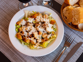 Fresh Caesar salad with chicken served on plate with serving pieces.