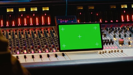 Music producer holding a tablet with greenscreen display on mixing console in control room,...