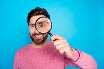 Cheerful man holding magnifying glass up to his eye against a vibrant blue background
