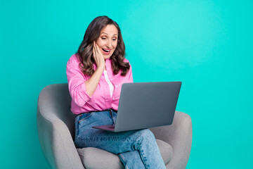 Photo of cheerful impressed lady dressed pink shirt sitting chair texting modern gadget empty space isolated turquoise color background