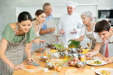 Adult male chef at master class teaches group of people how to cook food