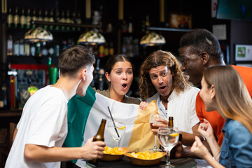 Emotional diverse soccer fans with flag of Ireland, rejoicing winning game with glasses of beer in the pub