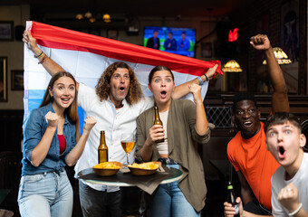 Fans with flag of Netherlands celebrate victory of their favorite team in a beer bar