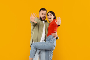 Obraz premium A young married couple expresses joy and affection in a playful pose, with the woman lifted by the man. Their bright smiles complement the vibrant yellow background, showcasing their love.